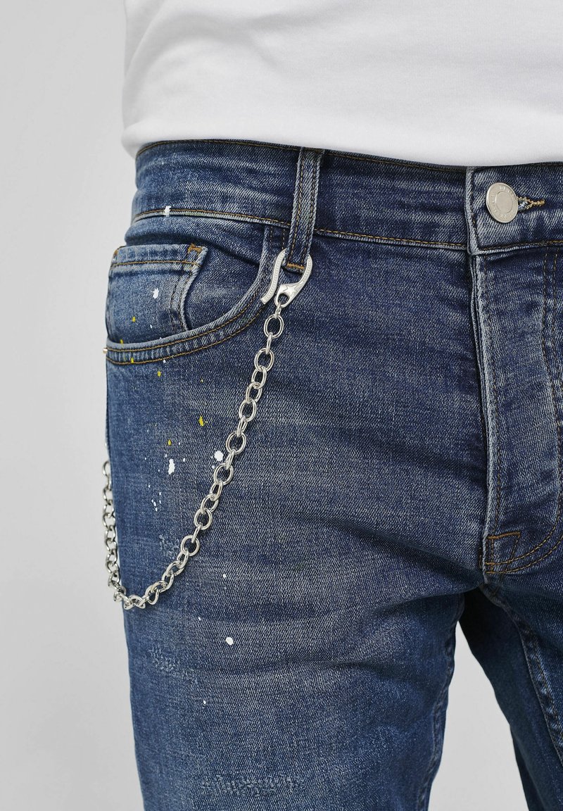Modré džíny z denimu s odstřiky barvy. Na poutku opasku je připevněn stříbrný řetěz s háčkovým detailem. Texturovaná látka a klasický design.