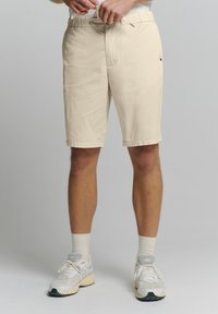 Beige, knielange shorts met een rechte snit en elastische tailleband. Voorzien van zijzakken en een klein logo aan de rechterkant.