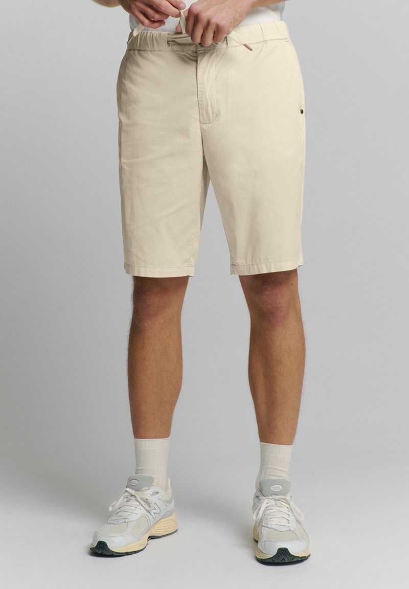 Beige, knielange shorts met een rechte snit en elastische tailleband. Voorzien van zijzakken en een klein logo aan de rechterkant.