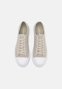 Baskets en toile beige avec capuchons en caoutchouc blanc, lacets plats et minimalisme à l'intérieur. Texture lisse, design classique à lacets.