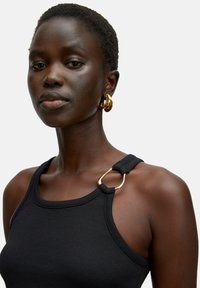 Zwarte geribbelde tanktop met een gouden metalen ringaccent op de schouderband, die een nauwsluitende pasvorm en zachte textuur benadrukt.