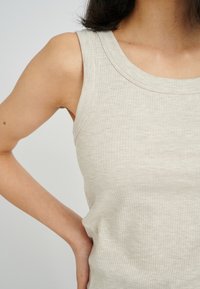 Ribbed beige sleeveless top with a round neckline and a fitted design. The fabric has a smooth texture and subtle stretch.