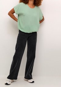 Helles grünes, locker sitzendes Blusenshirt mit kurzen Ärmeln; kombiniert mit hoch waisted, schwarzen weit geschnittenen Jeans und weißen Sneakers.