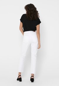 Jeans bianchi a vita alta con gamba dritta, design a cinque tasche e una patch in pelle marrone sulla vita posteriore. Abbinati a una maglietta nera.