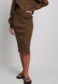 Stickad brun blyertskjol med vertikal ribbning, längd till mitten av vaden, sidan slits och resårmidja. Matchad med svarta flip-flop-sandaler.