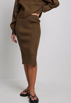 Gonna a matita marrone in maglia con rigature verticali, lunghezza a metà polpaccio, spacco laterale e vita elastica. Abbinata a ciabatte nere.