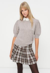 Light gray knitted sweater with short puff sleeves layered over a plaid skirt featuring brown and white tones. White collared shirt underneath.