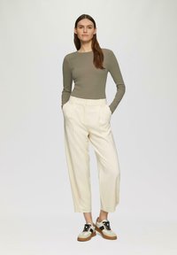 Licht olijfgroene geribbelde langemouwen top in combinatie met crèmekleurige wijde broek en multikleurige sneakers met lage schacht, wat een casual outfit toont.