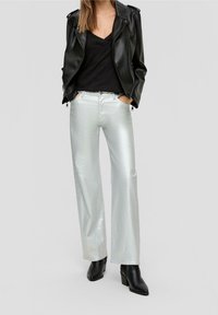 Blouson en cuir noir, haut à col en V noir et jeans large argent métallisé. Des bottines noires complètent la tenue.