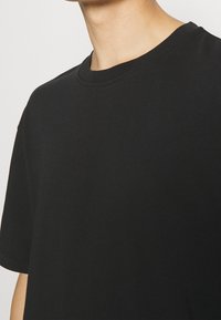 Černé bavlněné tričko s kulatým výstřihem, krátkými rukávy a volným střihem. Hladký povrch s jemnými švy na výstřihu.