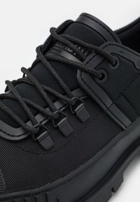 Zapatillas deportivas negras con parte superior de tejido texturizado, suela de goma y un sistema de cordones elegante con ojales moldeados y detalle del logo.