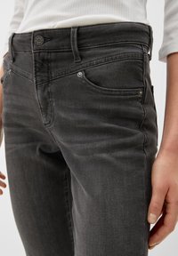 Jean en denim noir au design ajusté, doté de cinq poches, de quincaillerie métallique et d'une texture subtile sur le tissu. Finitions comprenant des coutures contrastées.