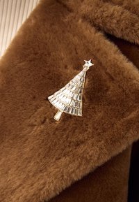 Brown faux-fur fabric with a shiny silver brooch shaped like a Christmas tree, featuring a star on top and a textured, geometric design.