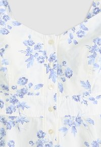 Tessuto bianco con stampa floreale azzurro chiaro, dotato di chiusura frontale con cinque piccoli bottoni bianchi su un indumento senza maniche.