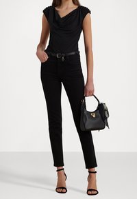 Svart topp med båtringning och rynkade axel detaljer, ihop med svarta högmidjade jeans och svarta sandaler med ankelsnörning, hållande en svart handväska.