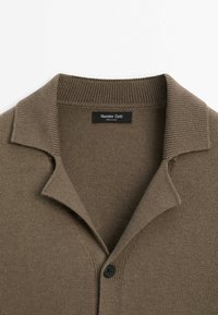 Cardigan tricoté taupe avec un col côtelé et une fermeture à boutons, doté d'une étiquette noire "Massimo Dutti" à l'intérieur de l'encolure.