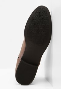 Ruskea nahkakenkä, jossa on teksturoitu musta kumipohja aaltoilevalla kuvioinnilla, suunniteltu pitävyyttä ja vakautta varten.