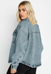 Överdimensionerad ljusblå denimjacka med fransad nederkant, bröstfickor och uppvikt ärmar. Har en klassisk krage och avslappnad passform.