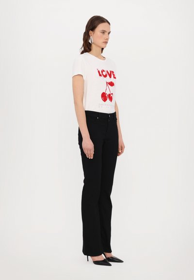 T-shirt bianco a maniche corte con testo rosso "LOVE" e grafica di ciliegie, abbinato a jeans flare neri e décolleté nere a punta.