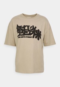 T-shirt beige à manches courtes avec de grands caractères asiatiques stylisés noirs et le texte "LOW LIGHTS STUDIOS" sur le devant.