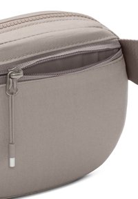 Grå tygpåse med en rundad design. Har en dragkedja och en strukturerad yta med en subtil glans. Dragkedjan har ett metalldrag.