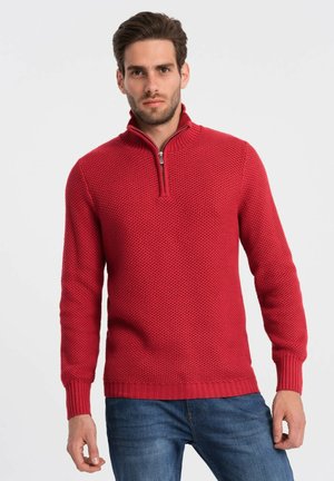 Sweater en tricot rouge avec un motif texturé, col zippé mi-hauteur et poignets et ourlet côtelés. Associé à un jean bleu, le design est décontracté et ajusté.