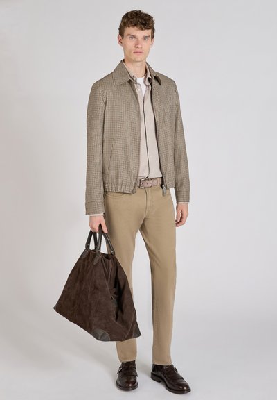 Chaqueta marrón a cuadros, camisa beige, pantalones marrón claro, bolso de ante marrón oscuro y zapatos oscuros. La chaqueta tiene una cremallera y un cuello alzado.