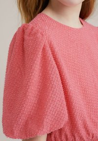 Blusa texturizada rosa con mangas cortas abullonadas, cuello redondo y patrones elevados intrincados en la tela.