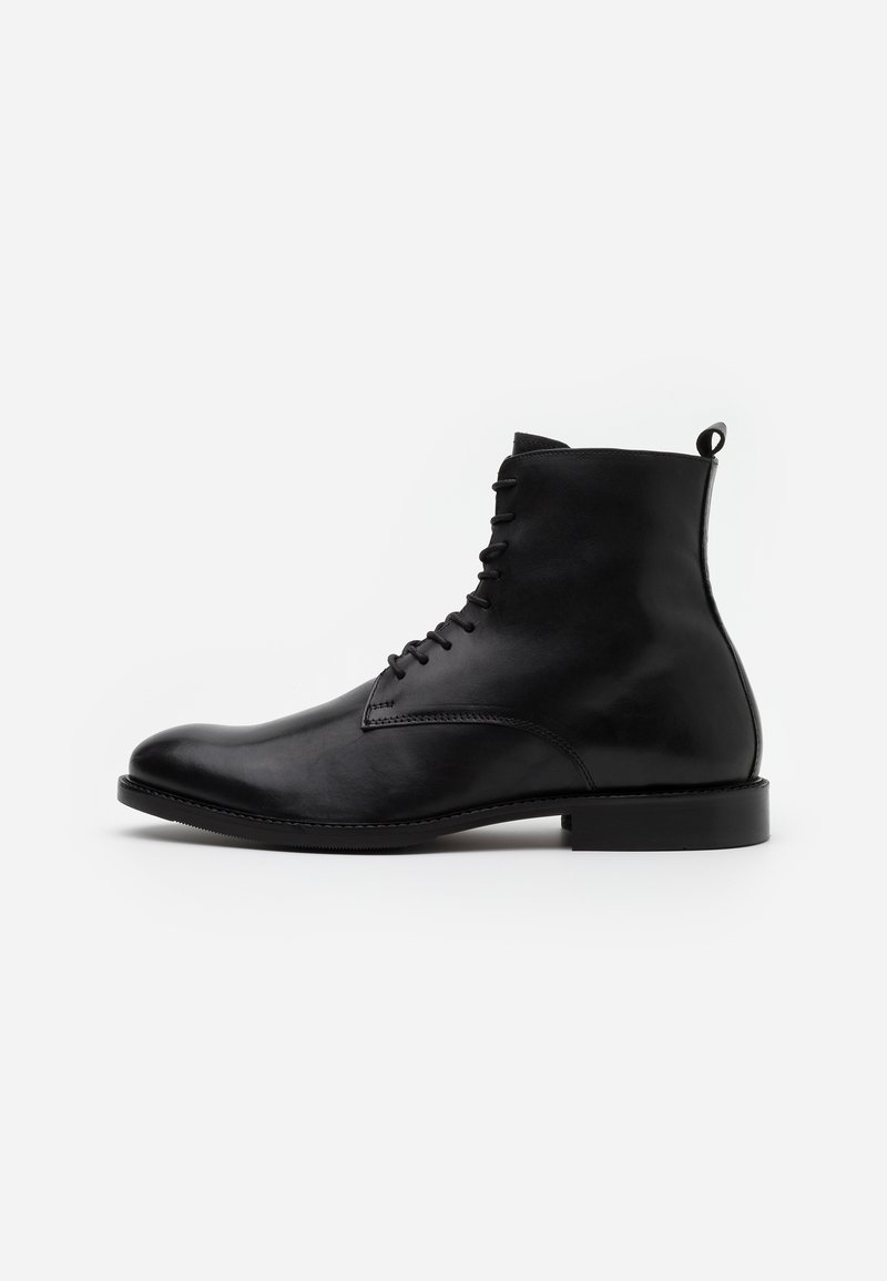 Botas de tobillo de cuero negro con un acabado suave, punta redonda, cordones en la parte frontal y una pequeña asa en la parte posterior. Suela de goma negra sólida.