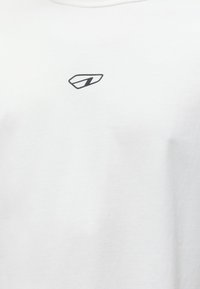Λευκό T-shirt με στρογγυλή λαιμόκοψη που διαθέτει ένα μικρό μαύρο γεωμετρικό λογότυπο στο κέντρο κοντά στη λαιμόκοψη.