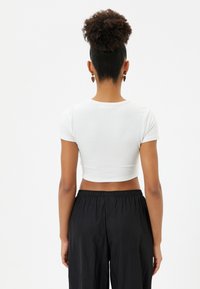 Camiseta blanca recortada de manga corta, con una textura suave y un diseño ajustado, combinada con pantalones negros holgados.