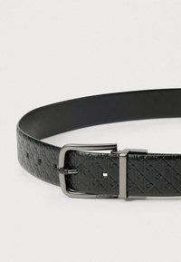 Μαύρη δερμάτινη ζώνη με ανάγλυφο σχέδιο και ορθογώνια αγκράφα ασημί απόχρωσης με ένα τετράγωνο διακοσμητικό. Ομαλή υφή.