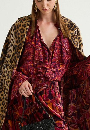 Leopard print coat, floral ruffled blouse in deep red and orange, matching smocked skirt, holding a black sequined handbag, shiny gold earrings.