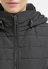 Černá vycpaná bunda s předním zipem, nastavitelnou kapucí a dvojicí předních kapes. Hladká textura s horizontálním prošíváním.