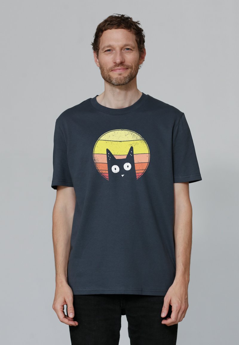 T-shirt en coton bleu foncé avec un graphisme d'un chat noir sur un design circulaire de coucher de soleil dans des tons jaunes, oranges et rouges.