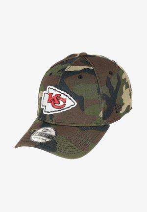 Berretto da baseball camouflage in tessuto, con una toppa bianca del logo di Kansas City, visiera curved e una vestibilità flessibile. I colori includono tonalità di verde e marrone.