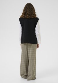 Crni vuneni prsluk s okruglim izrezom, slojevit preko bijele košulje, uparen s svijetlosivim kariranim hlačama širokih nogavica.