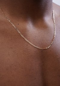 Goldene Kettenhalskette mit einem länglichen Glieddesign, die auf strukturiertem Haut liegen. Die Farbe ist reflektierend mit einer glatten Oberfläche.