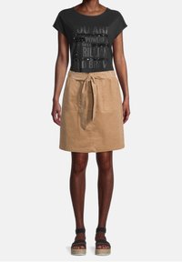 Svart t-shirt med paljetter och inspirerande text, kombinerad med en beige A-linje-formad kjol med knytmidja och framfickor.