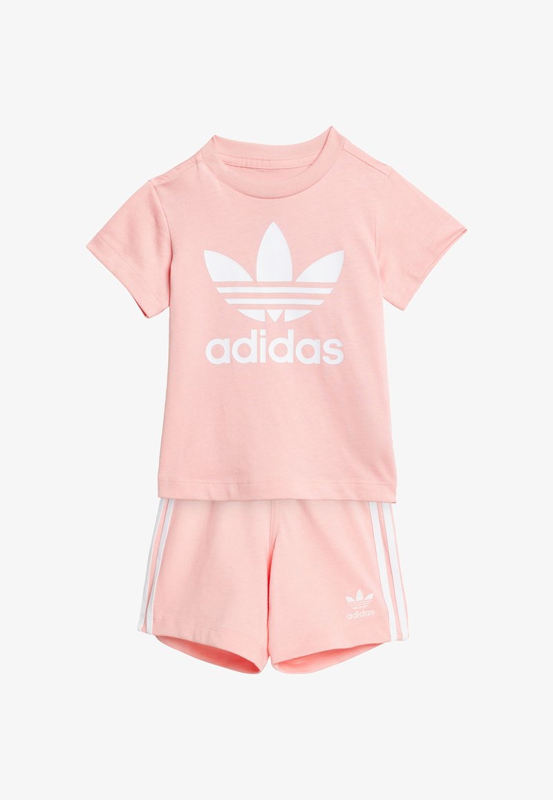 Camiseta de algodón rosa con el logo blanco de "adidas" y gráfico de trébol, combinada con pantalones cortos rosa a juego que tienen rayas laterales y logo blancos.