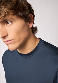 Mørkeblå tætsiddende langærmet skjorte med rund halsudskæring, glat tekstur og minimal syning ved kraven og skuldrene.