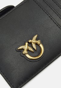 Schwarze Leder-Geldbörse mit strukturiertem Finish, ausgestattet mit einem goldfarbenen Metallring und zwei Vogelmotiven als markantem Akzent.