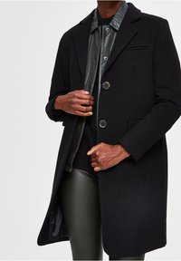 Schwarzer Wollmischungs-Mantel mit maßgeschneidertem Design, Reverskragen und Zwei-Knopf-Verschluss. Strukturiertes, glattes Futter und seitliche Taschen.