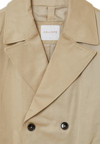 Beige Doppelreiher mit großen Revers, aus glattem Stoff gefertigt. Verfügt über zwei schwarze Knöpfe und ein Etikett mit der Aufschrift "CALLIOPE" innen.