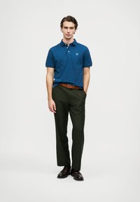 Navy blue polo shirt with a small logo, paired with green pants and brown leather shoes. The outfit features a classic collar and straight fit.