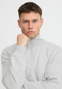 Grijze zip-up sweatshirt met een hoge kraag, geribbelde manchetten en een subtiele logodetail op de borst. Soepele textuur en casual ontwerp.