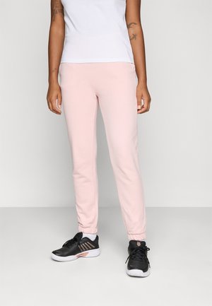 Pantalons de survêtement rose clair avec des poignets élastiques et des poches latérales, associés à des chaussures de sport noires avec des semelles blanches et des accents roses.