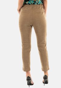 Pantaloni in velluto a coste marroni con un design aderente, cintura elastica e due tasche posteriori; texture liscia e stile a gamba affusolata.