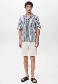 Korte mouwen gestreept shirt in blauw en wit, gemaakt van lichtgewicht stof. Gecombineerd met witte shorts en zwarte slide sandalen.