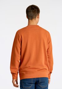Oranje sweatshirt met lange mouwen, geribbelde manchetten en zoom, ronde hals en zachte textuur, gecombineerd met blauwe jeans.